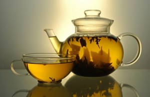 Glass teapot and cup with green tea on grey background